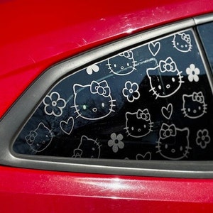 May include: A red car with a black window that has a pattern of Hello Kitty faces and hearts on it.
