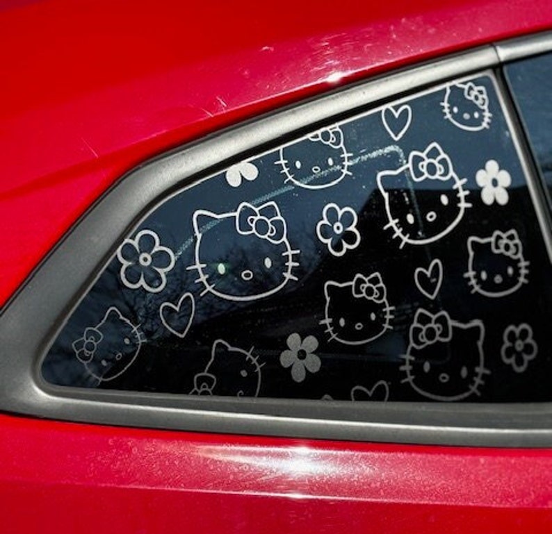 May include: A red car with a black window that has a pattern of Hello Kitty faces and hearts on it.