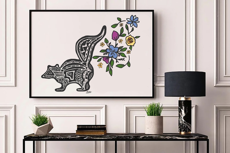以下が含まれることがあります： 白黒の線画で描かれた、スタイリッシュなスカンクのイラスト。尻尾は花束になっており、黄色、青、紫、緑の花が咲いています。作品は額装され、白い壁に飾られています。