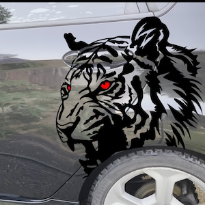 May include: Black and white tiger head decal with red eyes, applied to the side of a black car. The decal is a silhouette of a tiger's head with a fierce expression.