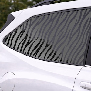 May include: White car with a rear window featuring a zebra stripe pattern. The black and gray design covers the window, offering a decorative and stylish look. The car's taillight is visible.