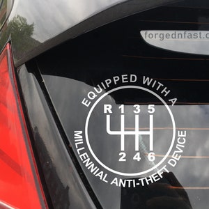 Puede incluir: Calcoman&iacute;a blanca en la ventana de un coche con un diagrama de cambio de marchas y el texto &laquo;EQUIPPED WITH A MILLENNIAL ANTI-THEFT DEVICE&raquo;. Tambi&eacute;n se ve el sitio web &laquo;forgednfast.com&raquo;. El piloto trasero del coche es rojo.