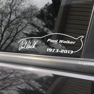 May include: White vinyl decal on a car window with a silhouette of a car and the text "Paul Walker 1973-2013".