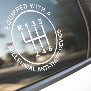 Puede incluir: Calcoman&iacute;a blanca en la ventana de un coche con un patr&oacute;n de cambio de marchas y el texto "EQUIPPED WITH A MILLENNIAL ANTI-THEFT DEVICE". El dise&ntilde;o incluye los n&uacute;meros y posiciones de una transmisi&oacute;n manual de seis velocidades.