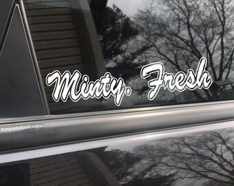 May include: White vinyl sticker with the text "Minty. Fresh" on a black car window.