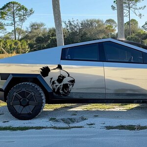 May include: A silver pickup truck with a black panda bear decal on the side. The truck has black wheels and a black interior.