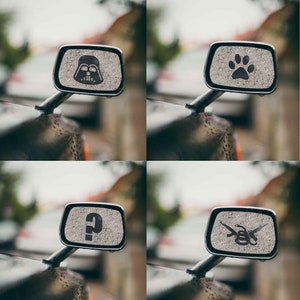 May include: Four car side view mirrors with different decals. The first mirror has a Darth Vader decal, the second has a paw print, the third has a question mark, and the fourth has a snake with crossed pistols.