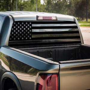 May include: A black pickup truck with a black and white American flag decal on the rear window.