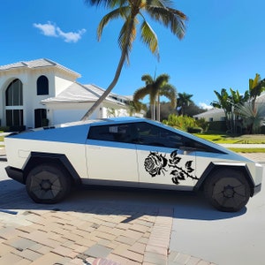 May include: A futuristic, white and light blue electric vehicle with a black rose decal on the side. The vehicle has a unique angular design and black wheels. The background features a sunny day with palm trees and a residential neighborhood.