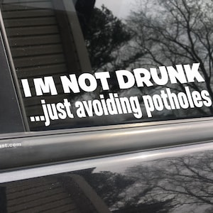 May include: White vinyl sticker on a black car window that reads "I'M NOT DRUNK...just avoiding potholes".
