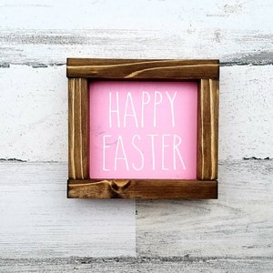 May include: A wooden frame with a pink background and the text "HAPPY EASTER" in white lettering.
