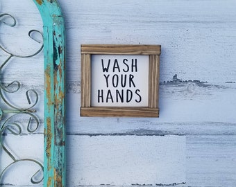 May include: A wooden sign with the text "WASH YOUR HANDS" in black lettering on a white background. The sign is framed in a rustic brown wood frame.