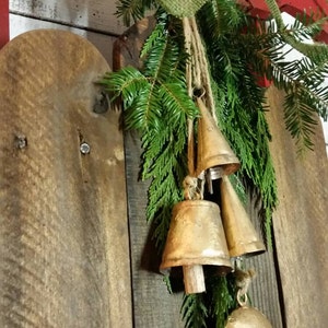 May include: A rustic Christmas decoration featuring a red wooden sled with a green burlap bow and evergreen branches. Gold-colored bells hang from the branches, creating a festive holiday display.