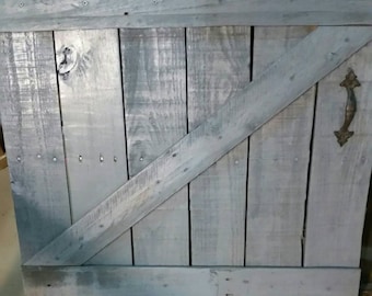 Könnte beinhalten: Eine rustikale Holztür mit diagonalem Planken-Design. Die Tür ist in einem hellen Grauton gestrichen und hat einen Metallgriff.