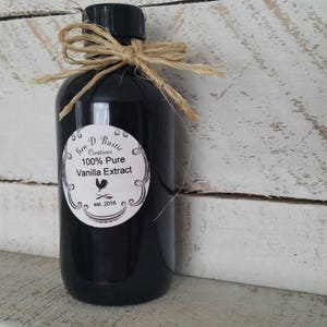 May include: A black glass bottle with a white label that reads "Gem D Rustic Creations 100% Pure Vanilla Extract est. 2016". The bottle is tied with twine and a bow.