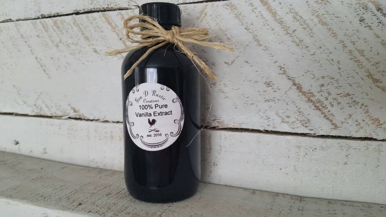 May include: A black glass bottle with a white label that reads "Gem D Rustic Creations 100% Pure Vanilla Extract est. 2016". The bottle is tied with twine and a bow.