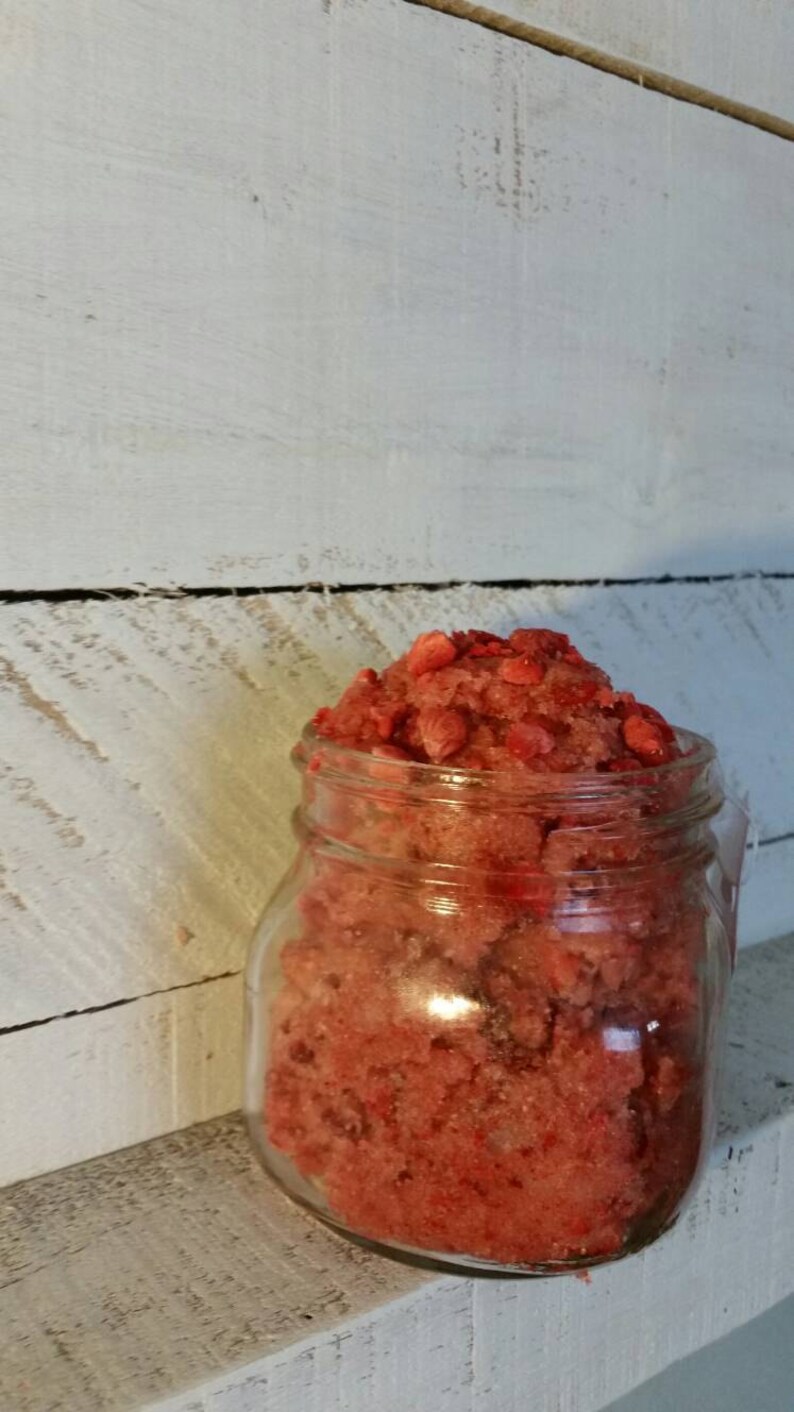May include: A glass jar filled with a red and white sugar scrub. The scrub is made with sugar and fresh strawberries.