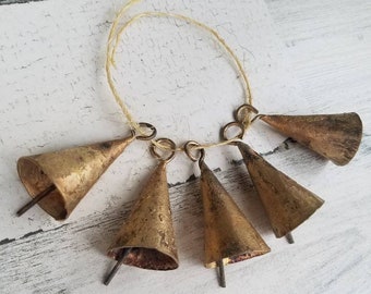 May include: A set of six gold-toned jingle bells tied together with twine. The bells are cone-shaped and have a rustic, aged look.