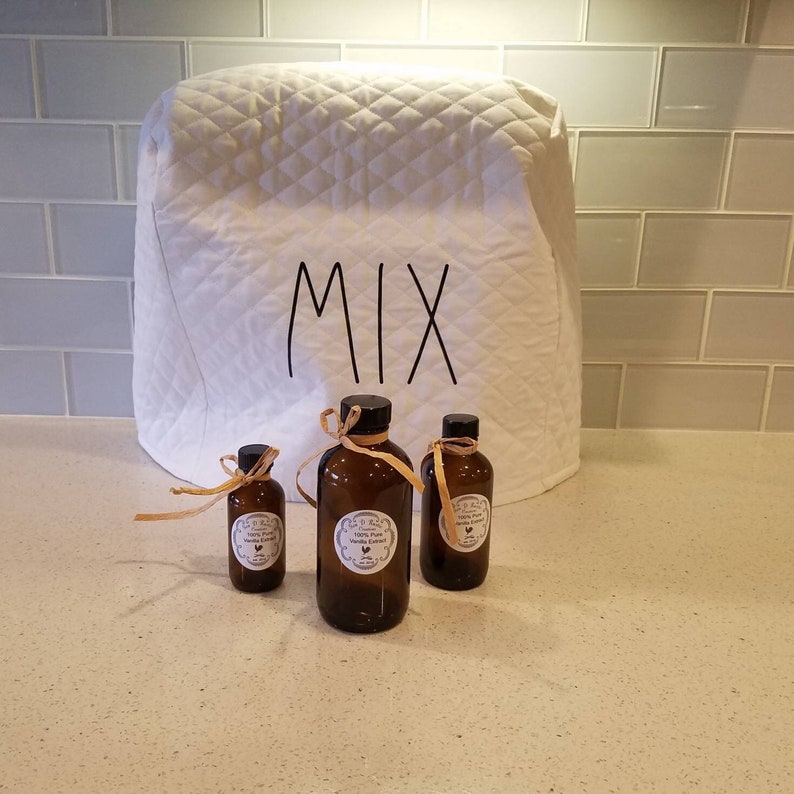 May include: Three glass bottles with brown labels that say "100% Pure Vanilla Extract" and a white label that says "Mix" on a white quilted kitchen appliance cover.