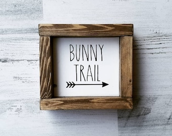 Puede incluir: Un letrero de madera con fondo blanco y texto negro que dice "Bunny Trail" con una flecha negra apuntando hacia la derecha.