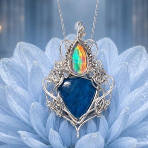 May include: A silver wire-wrapped pendant necklace featuring a teardrop-shaped iridescent opal at the top and a larger, triangular deep blue stone at the base. The intricate metalwork surrounds both stones, suspended from a delicate silver chain.