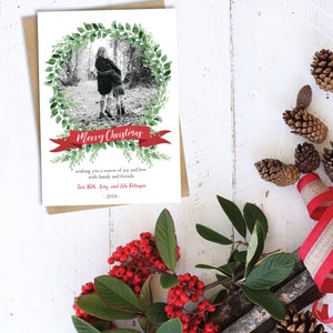 May include: A black and white photo of two children standing in a wooded area is framed by a green wreath with a red ribbon that reads "Merry Christmas". The text below the wreath reads "wishing you a season of joy and love with family and friends Tory, Beth, Arty, and Isla Peterson - 2018 - "