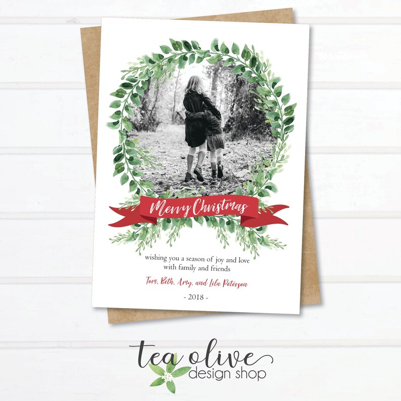 May include: A Christmas card with a watercolor wreath of green leaves surrounding a black and white photo of two children. The card has a red ribbon with the text "Merry Christmas" and a message wishing a season of joy and love with family and friends. The card is signed with the names Torr, Beth, Arry, and Lila Peterson and the year 2018.
