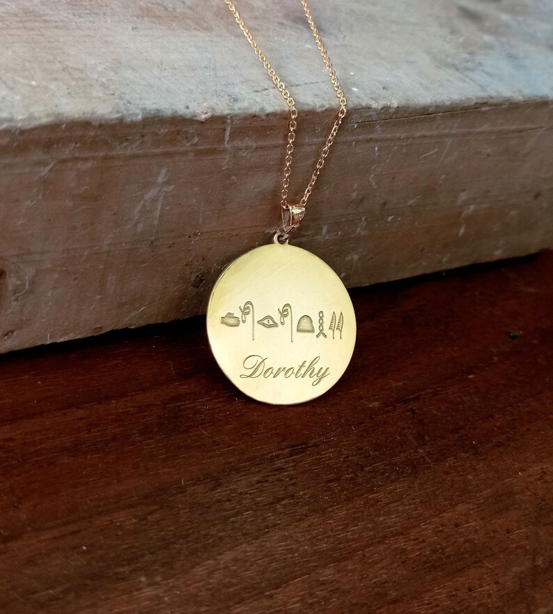 May include: Gold necklace with a round pendant featuring the name "Dorothy" engraved in cursive script and a row of ancient Egyptian hieroglyphs above the name.