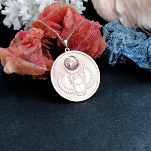 May include: Silver necklace with a pendant featuring a scarab beetle with wings, a crescent moon, and the Eye of Horus. The pendant is on a black background.