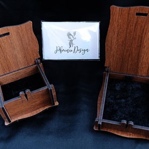 K&ouml;nnte beinhalten: Zwei Holzkisten mit ge&ouml;ffneten Deckeln, die schwarze Samt-Innenseiten zeigen. Die Kisten sind aus hellem braunem Holz mit einer dunkelbraunen Beize. Die Kisten sind beide rechteckig und haben ein dekoratives Design auf der Vorderseite. Die Kisten stehen auf einer schwarzen Oberfl&auml;che. Der Text "Phoenix Design" ist auf einer wei&szlig;en Karte im Hintergrund sichtbar.