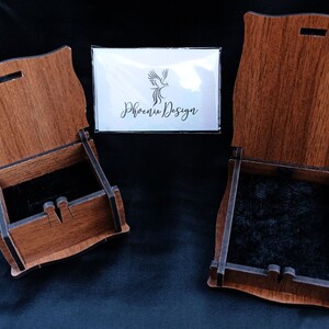 May include: Two wooden boxes with lids open, revealing black velvet interiors. The boxes are made of light brown wood with a dark brown stain. The boxes are both rectangular in shape and have a slightly curved top. The boxes are sitting on a black surface. The text "Phoenix Design" is visible on a white card in the background.