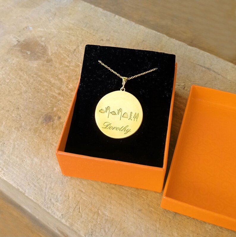 May include: Gold necklace with a round pendant featuring hieroglyphics and the name "Dorothy" engraved on it. The necklace is in a black and orange gift box.