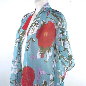 May include: A turquoise kimono with a floral design. The pattern includes large red flowers, white blossoms, and purple butterflies. The garment is displayed on a mannequin against a white backdrop. The fabric is sheer.