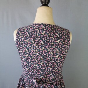 May include: A sleeveless dress with a floral pattern, displayed on a mannequin. The dress features a dark navy blue background with a delicate pattern of pink, white, and yellow flowers. A bow detail is visible at the waist, adding a feminine touch.