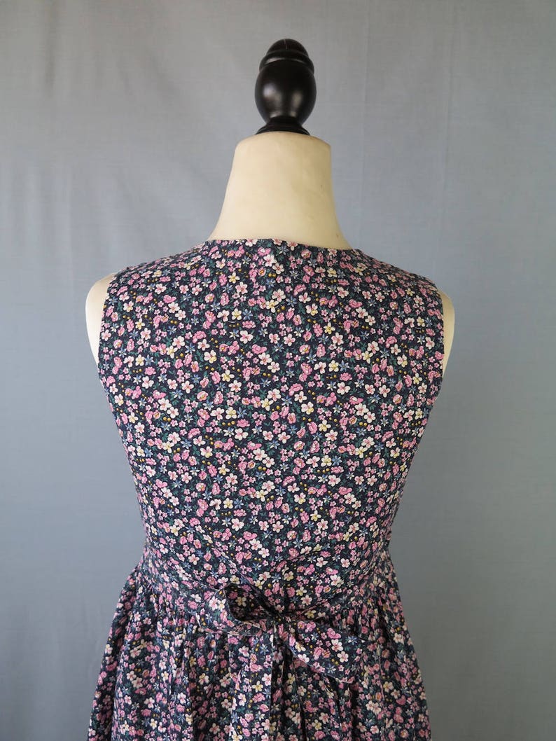 May include: A sleeveless dress with a floral pattern, displayed on a mannequin. The dress features a dark navy blue background with a delicate pattern of pink, white, and yellow flowers. A bow detail is visible at the waist, adding a feminine touch.