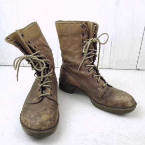 May include: A pair of worn, brown leather combat boots with laces. The boots have a distressed appearance, showing signs of wear and tear. The laces are a lighter shade of brown, and the soles are a darker brown.