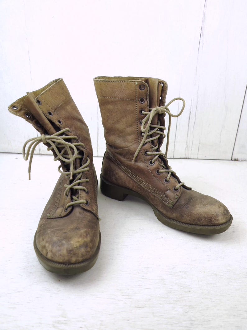 May include: A pair of worn, brown leather combat boots with laces. The boots have a distressed appearance, showing signs of wear and tear. The laces are a lighter shade of brown, and the soles are a darker brown.