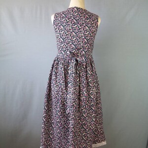 May include: A sleeveless floral print dress on a mannequin. The dress features a dark navy background with a pattern of small pink, white, and light blue flowers. It has a fitted bodice, a gathered skirt, and a white lace trim at the hem.