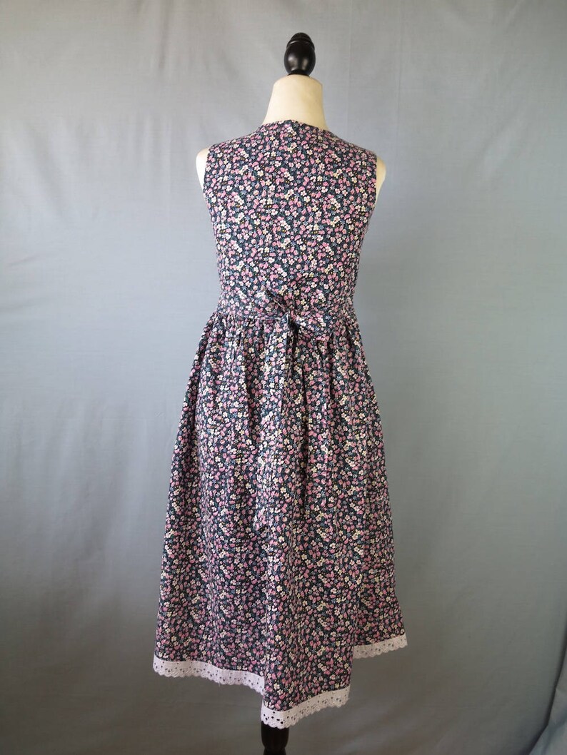 May include: A sleeveless floral print dress on a mannequin. The dress features a dark navy background with a pattern of small pink, white, and light blue flowers. It has a fitted bodice, a gathered skirt, and a white lace trim at the hem.