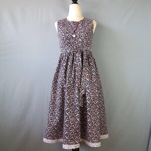 May include: A sleeveless, floral-print dress on a mannequin. The dress features a dark background with a pattern of small pink and white flowers. It has a fitted bodice, a button-up front, and a flared skirt with a lace trim at the hem.