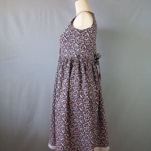 May include: A sleeveless floral print dress with a scoop neckline and a gathered skirt. The dress features a dark navy background with small pink and white flowers. The hemline is trimmed with white lace. A bow detail is visible at the back.