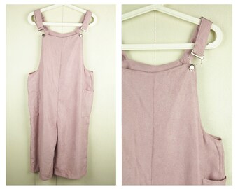 May include: A dusty rose-colored overall jumpsuit with adjustable straps and metal hardware. The garment features two front pockets and is hanging on a white hanger. The fabric appears to be a lightweight linen or cotton blend.