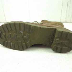 May include: Close-up of the sole of a tan combat boot. The olive green sole has a deep tread pattern for grip. The boot's upper is a light brown color, and the laces are visible. The boot is set against a white background.