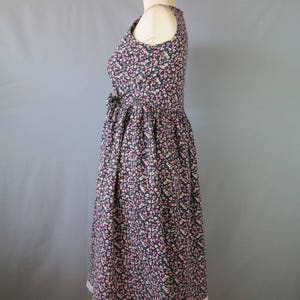 May include: A sleeveless floral print dress on a mannequin. The dress features a dark blue background with a pattern of small pink and white flowers. The skirt has a white lace trim at the hem. The dress is fitted at the bodice and flares out at the waist.