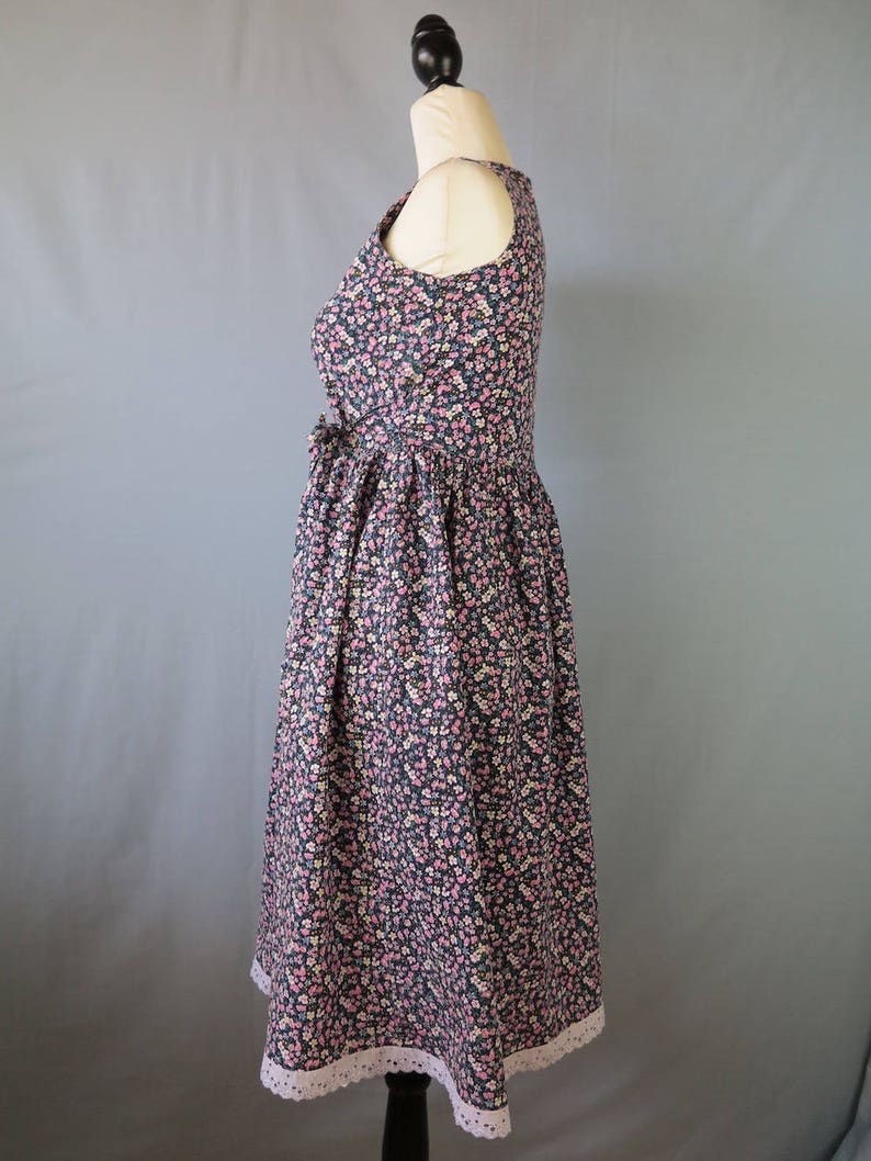 May include: A sleeveless floral print dress on a mannequin. The dress features a dark blue background with a pattern of small pink and white flowers. The skirt has a white lace trim at the hem. The dress is fitted at the bodice and flares out at the waist.