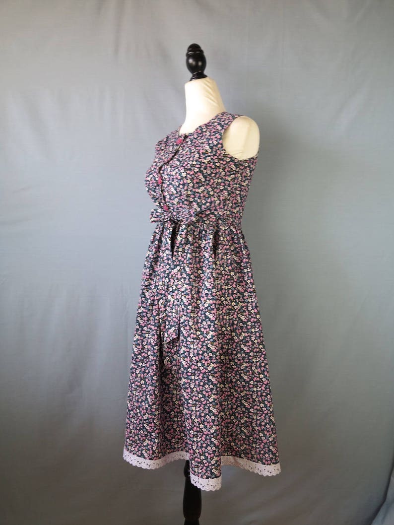 May include: A sleeveless floral print dress with a navy blue background and small pink and white flowers. The dress has a fitted bodice, a bow at the waist, and a white lace trim at the hem.