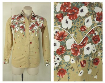 May include: A tan button-down shirt with a floral pattern. The shirt has a white collar and cuffs, and the yoke and front panels are decorated with red and white flowers. The overall design includes small red and white floral accents.