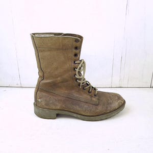May include: A worn, olive-green combat boot with a lace-up design. The boot features a scuffed leather exterior, metal eyelets, and a sturdy sole. The boot is a vintage style, suitable for outdoor activities.