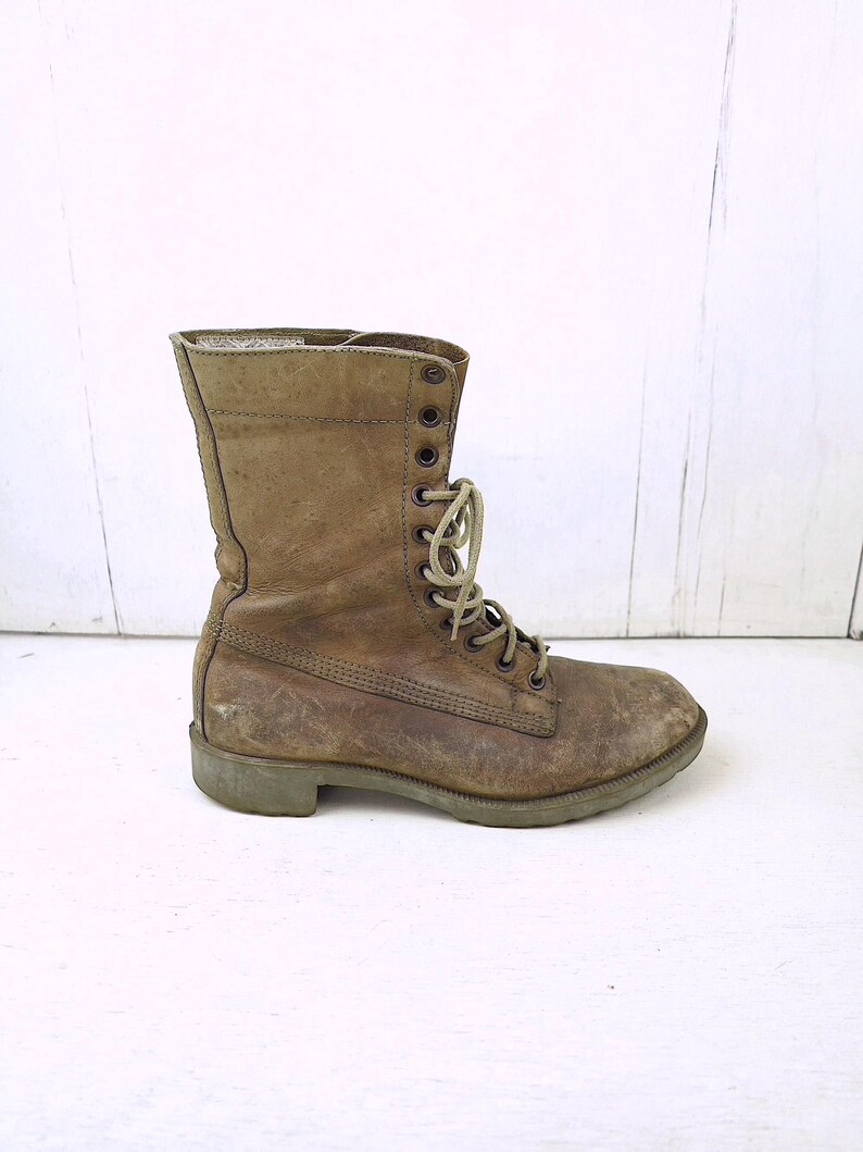 May include: A worn, olive-green combat boot with a lace-up design. The boot features a scuffed leather exterior, metal eyelets, and a sturdy sole. The boot is a vintage style, suitable for outdoor activities.