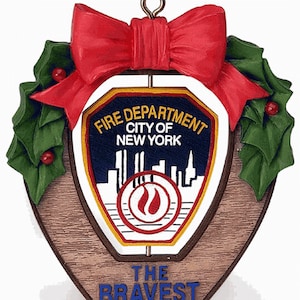 May include: A red and green Christmas ornament featuring the New York City Fire Department logo with the words "Fire Department City of New York" and "The Bravest" on a wooden background.